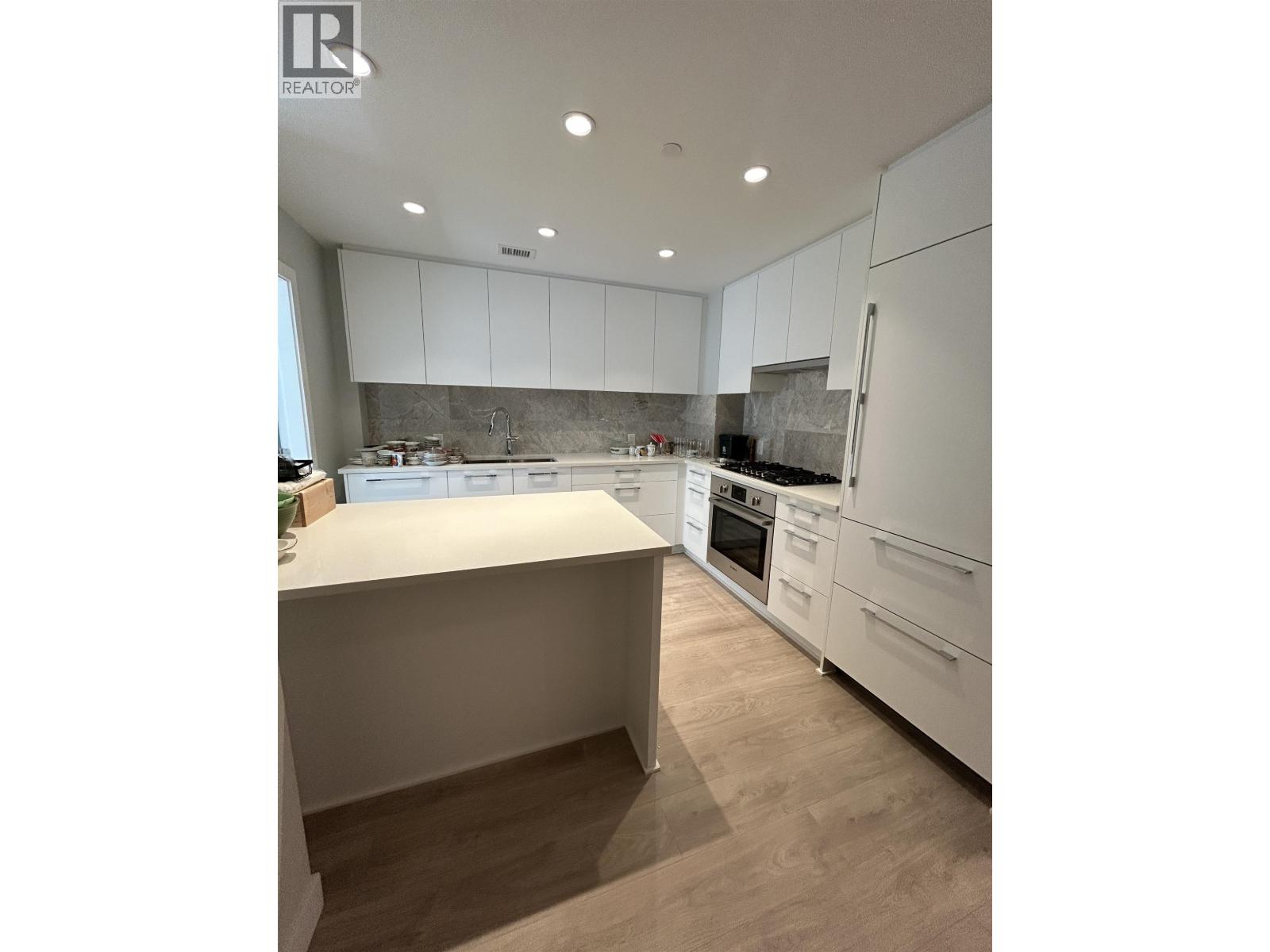 A modern kitchen with white cabinets and a wooden floor.