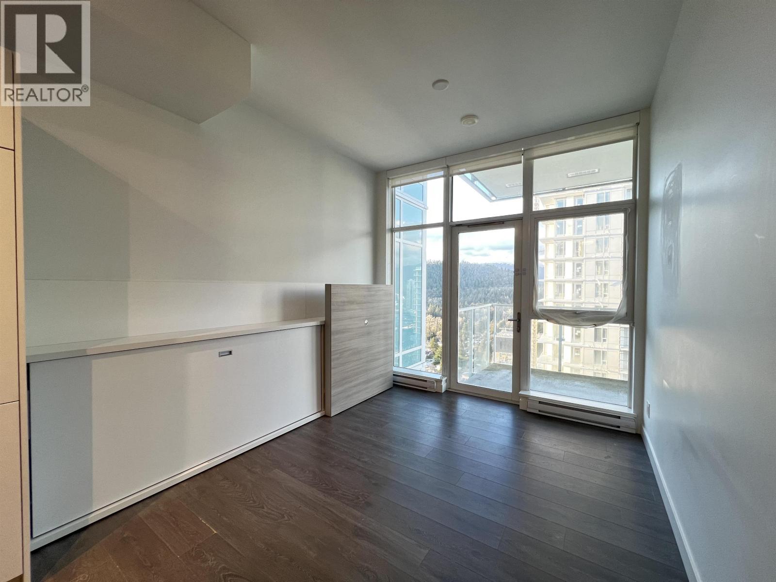 A spacious room with wooden floors and large windows overlooking a cityscape.