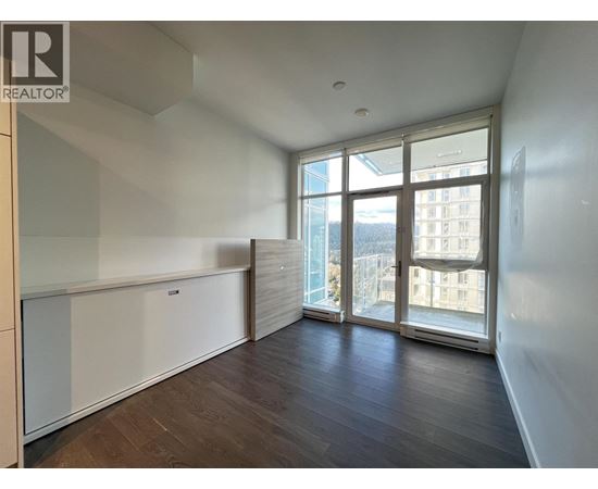 A spacious room with wooden floors and large windows overlooking a cityscape.