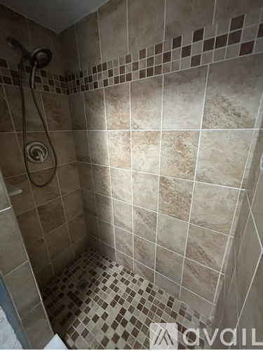 A tiled shower with a shower head and a drain.