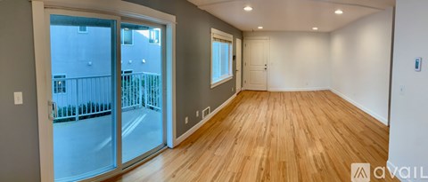 A room with wooden floors and a sliding glass door leading to a balcony.