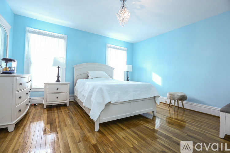 A bedroom with a white bed, dresser, and nightstand with a chandelier hanging from the ceiling.
