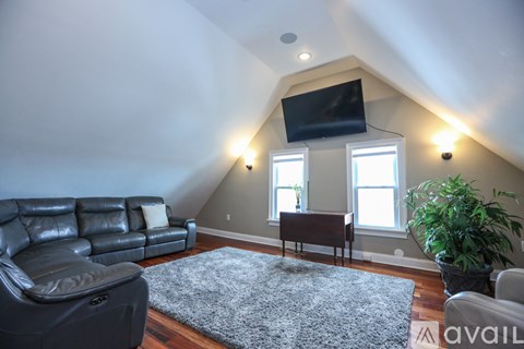 A living room with a black leather couch and a grey rug.