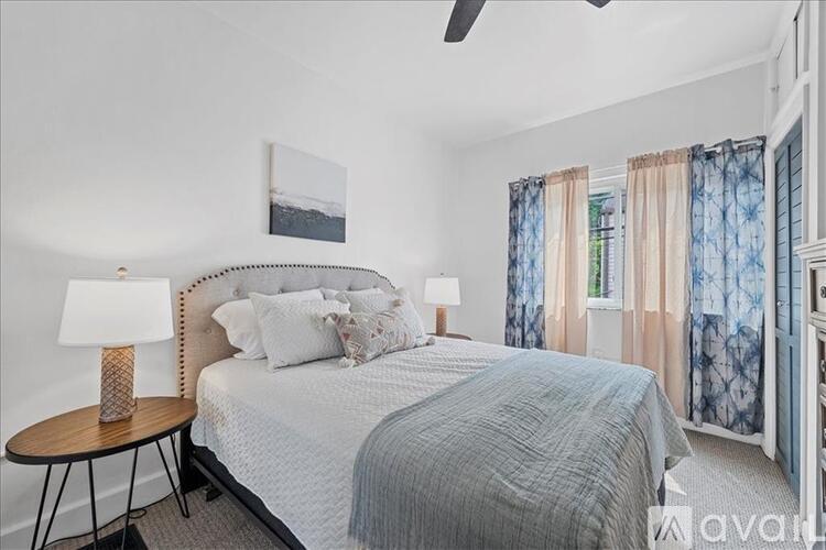 A bedroom with a bed, a round table with a lamp, and a ceiling fan.