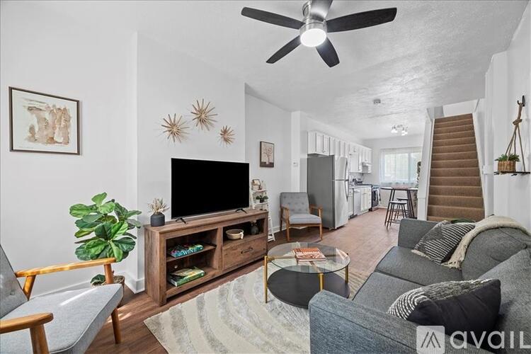 A living room with a grey couch, a wooden entertainment center, and a staircase in the background.