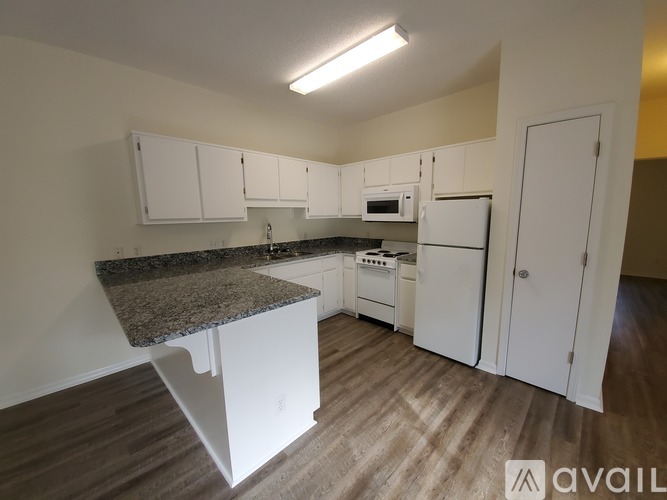 A kitchen with white cabinets and appliances, a granite countertop, and a wooden floor.