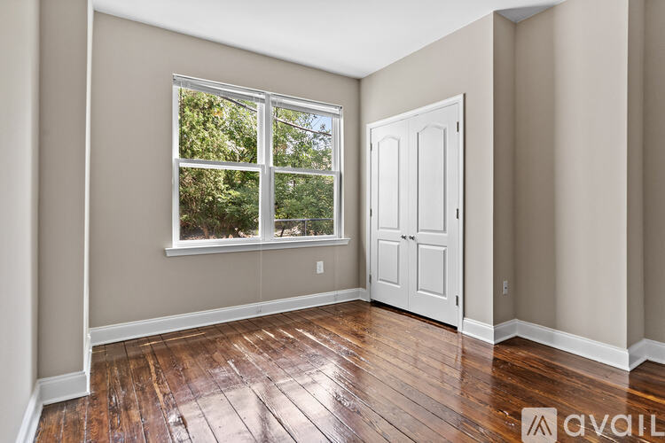 A room with a white door and a window with a view of trees.