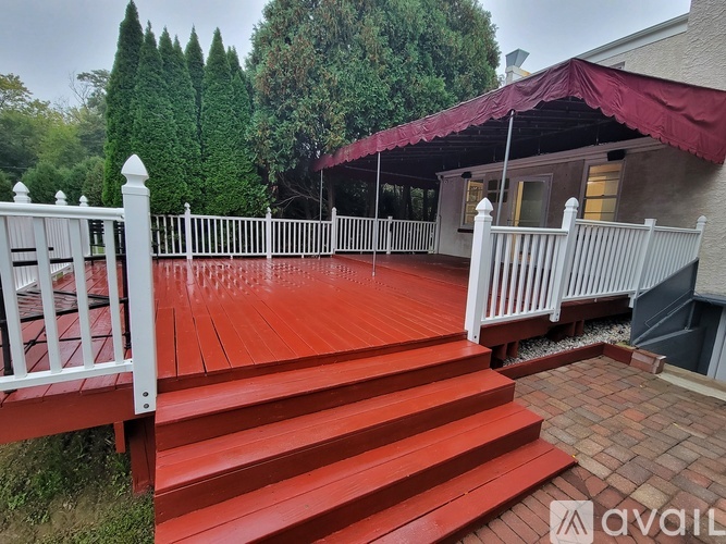 A red wooden deck with white railings and a white house in the background.
