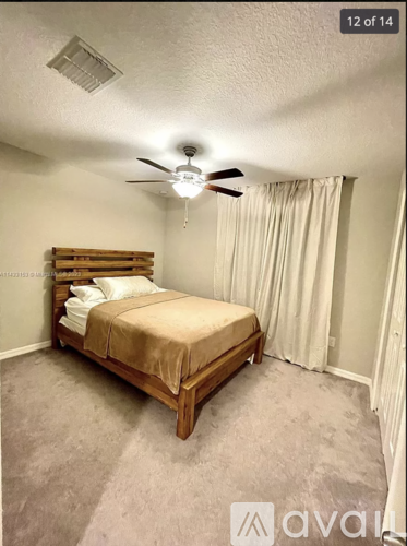 A bedroom with a bed, fan, and carpeted floor.