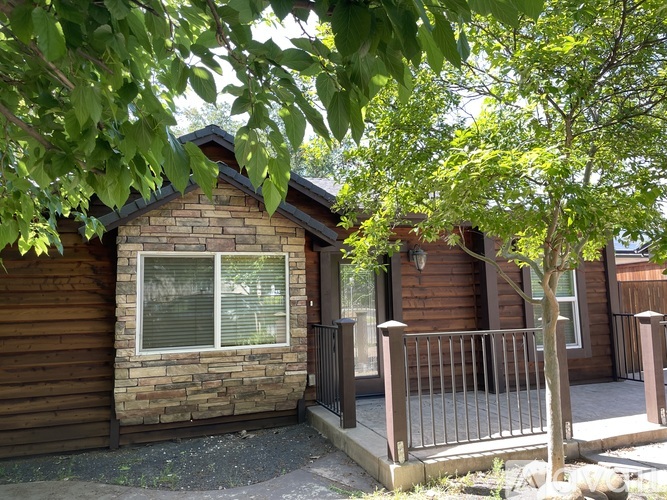 A small brown house with a porch and a tree in front.