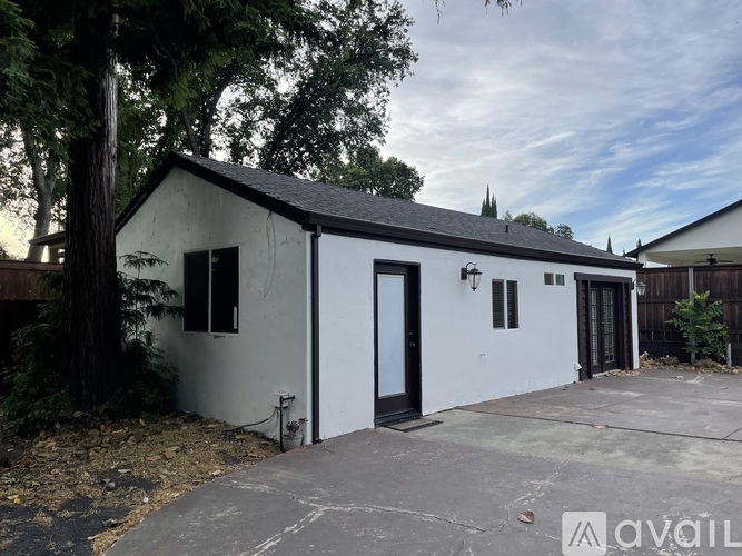 A white building with a black door and windows surrounded by trees.