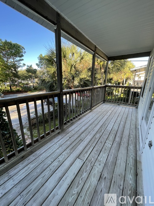 A wooden deck with a metal railing and a view of trees and a building in the background.