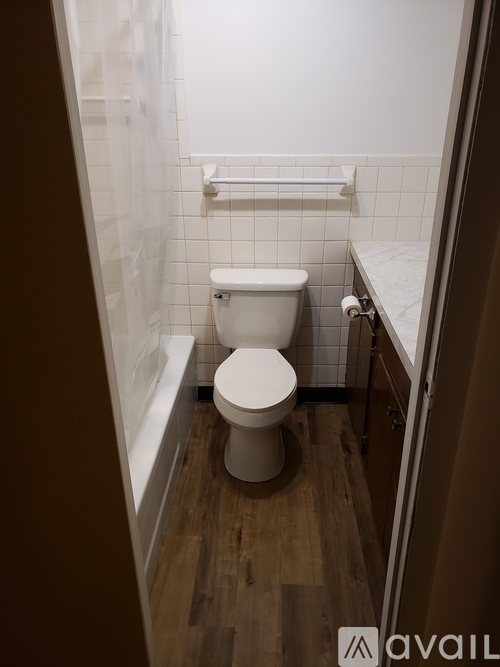 A white toilet sits in a bathroom with a wooden floor and white tiles.