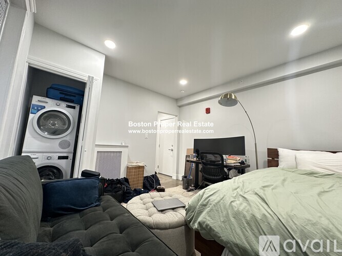 A bedroom with a bed, a washing machine, and a desk.