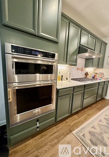 A modern kitchen with a stainless steel oven and green cabinets.