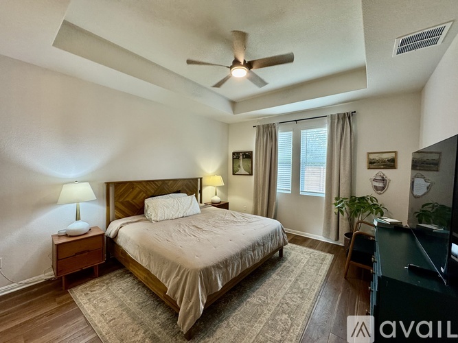 A bedroom with a large bed, a ceiling fan, and a window with curtains.
