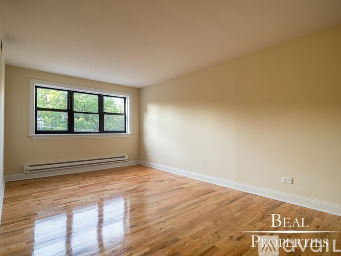 A room with wooden floors and a window showing trees outside.