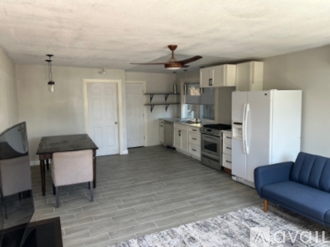 A living room with a blue couch and a kitchen area with white appliances.