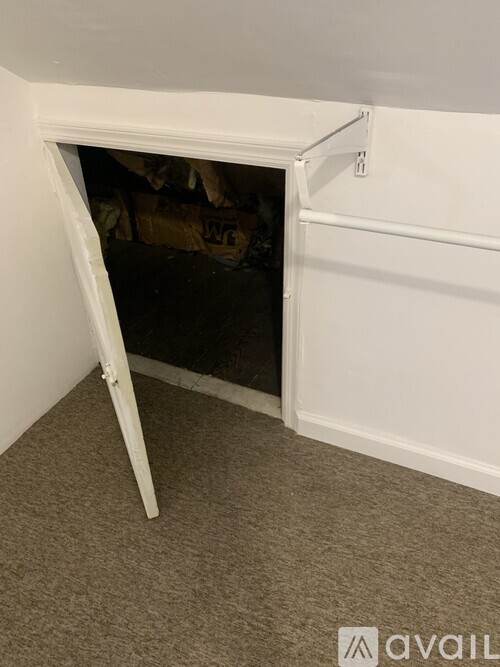 A white tripod stands in a corner of a room with a doorway leading to a cluttered space.