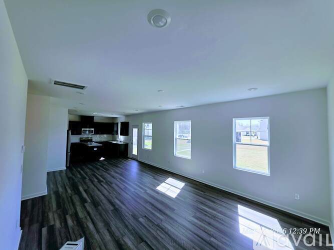 A spacious room with wooden floors and three windows letting in natural light.