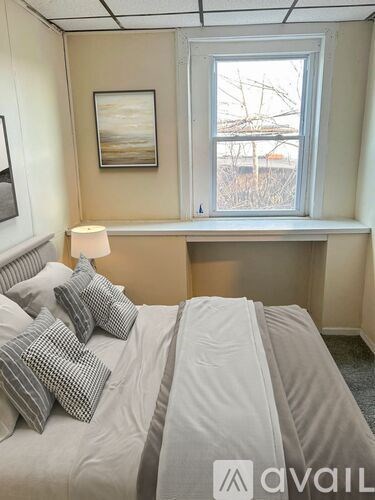 A bedroom with a bed, pillows, a nightstand, and a window.