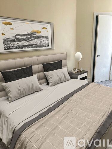 A bed with a grey headboard and a painting above it.