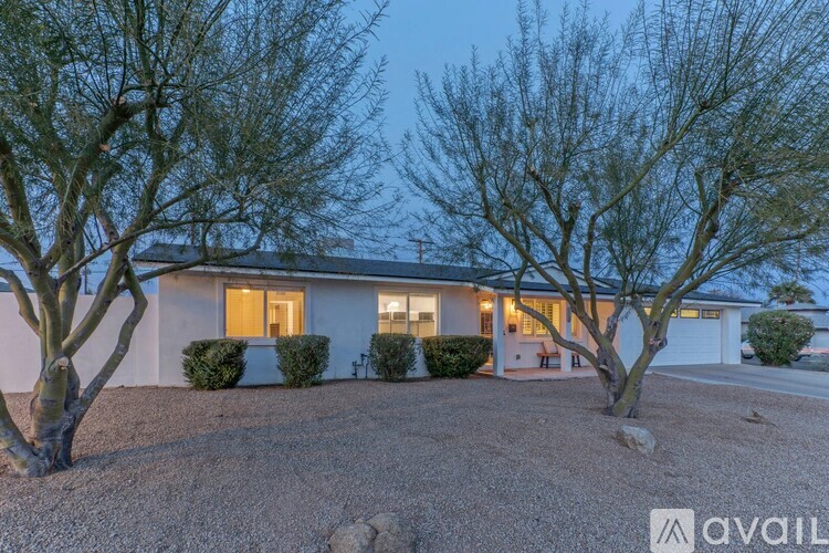 A house with a gravel driveway and two trees in front.