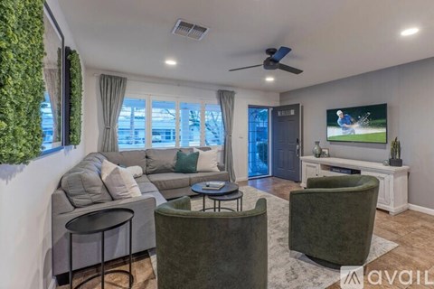 A living room with a grey sofa, a green armchair, and a television playing a golf game.