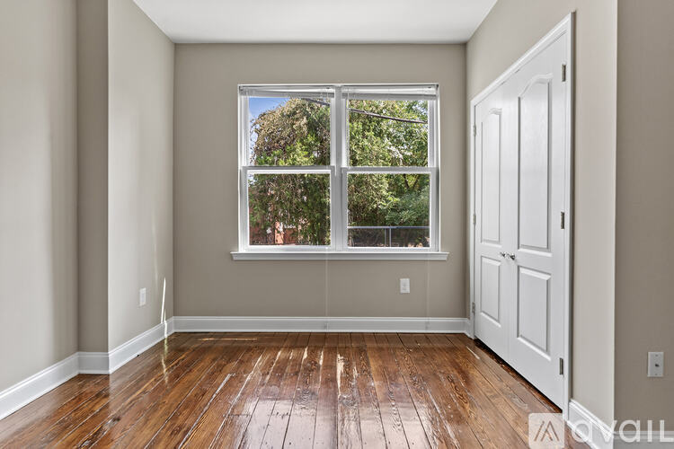 A room with a white door and a window with a view of trees.