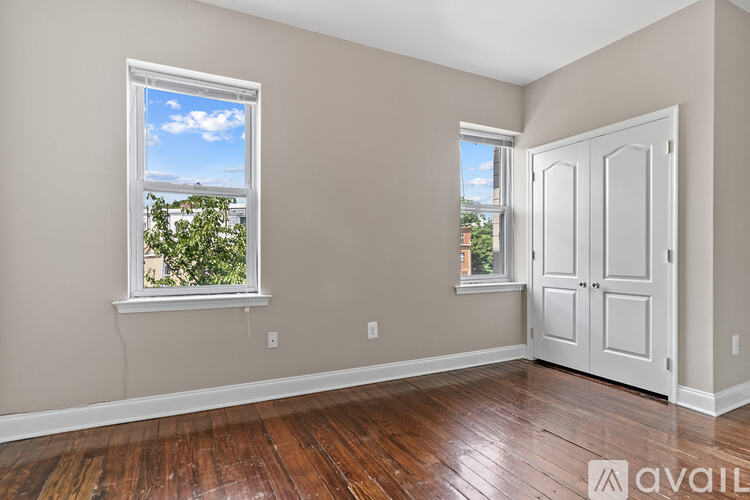 A room with a wooden floor, two windows, and a door.