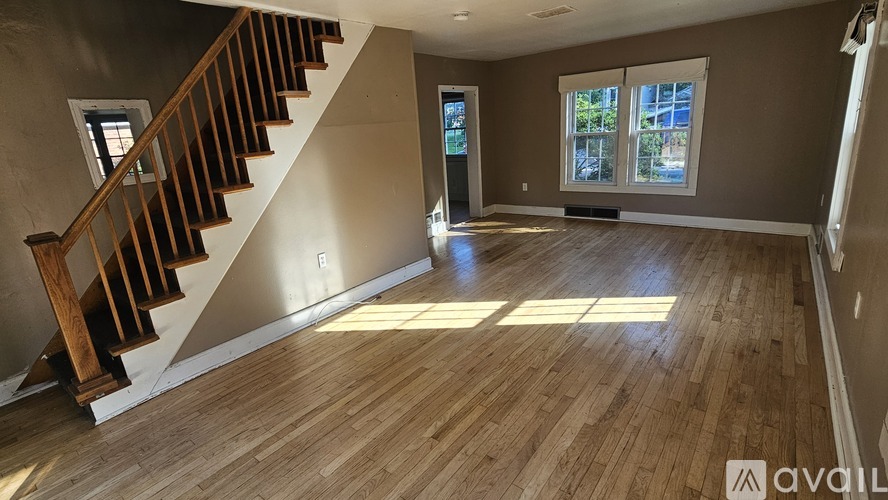 A spacious room with wooden flooring and a staircase leading to another level.