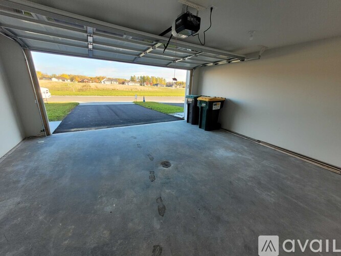 A spacious garage with a blue tarp on the floor and two green bins on the wall.