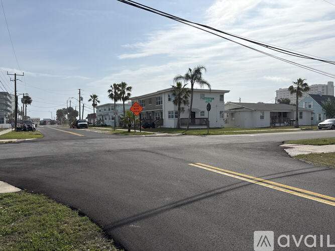 A street view with a road, a house, and a palm tree.