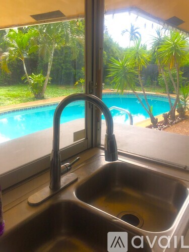 A kitchen sink with a window view of a pool and trees.