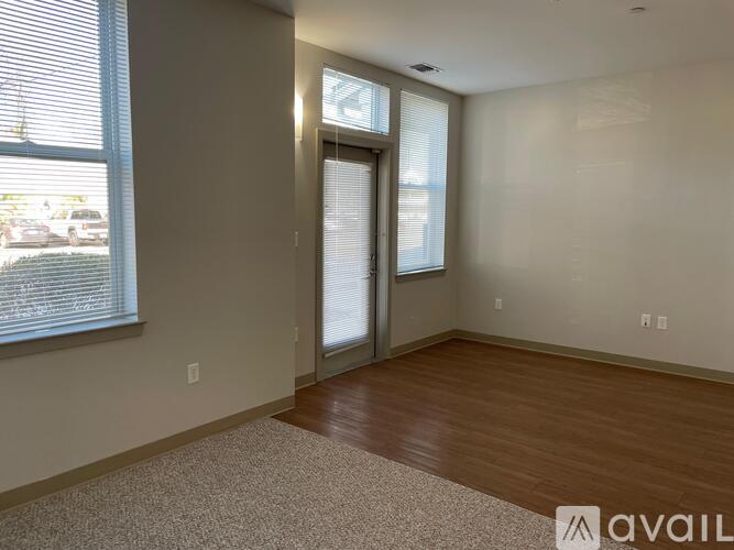 A room with a carpeted floor, a window with blinds, and a door leading to another room.