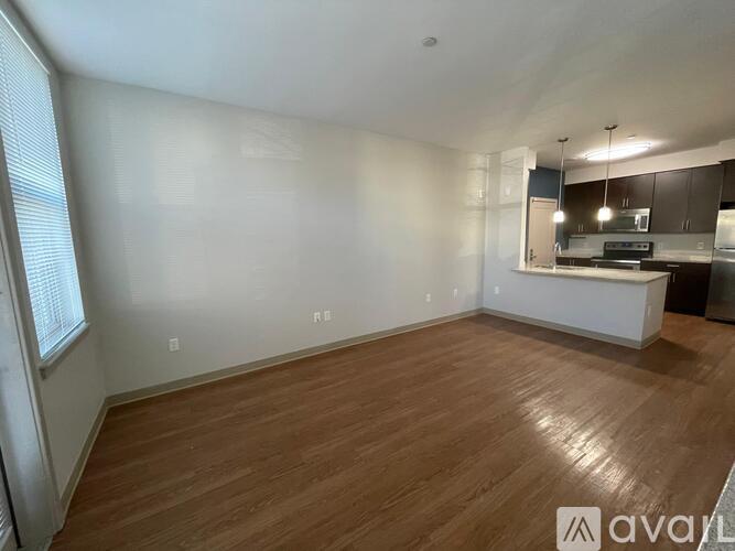 A spacious room with wooden flooring and a kitchen area in the background.