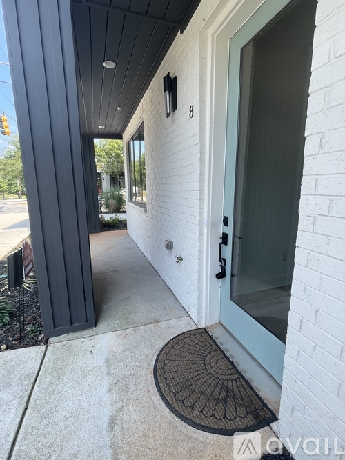A white house with a black door and a black mat on the concrete.