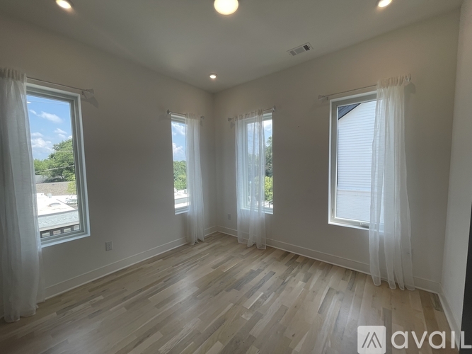 A spacious room with wooden flooring and three windows with white curtains.