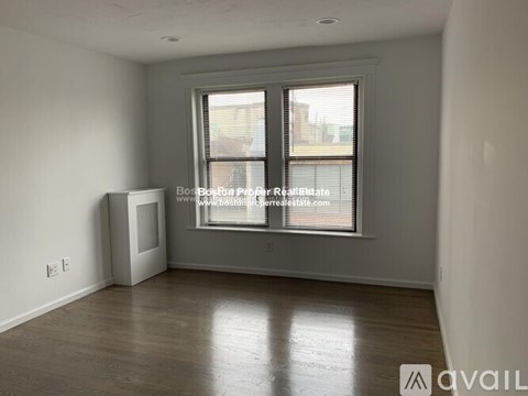 A spacious room with a large window and wooden flooring.