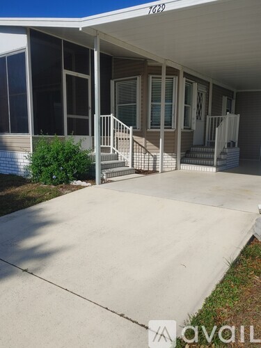 A concrete patio area in front of a house with a white railing and steps leading to the front door.