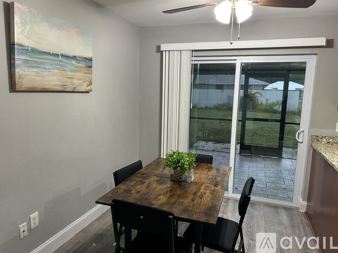 A dining room with a wooden table and chairs, a ceiling fan, and a painting on the wall.