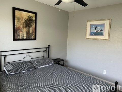 A bedroom with a bed, a ceiling fan, and two pictures on the wall.