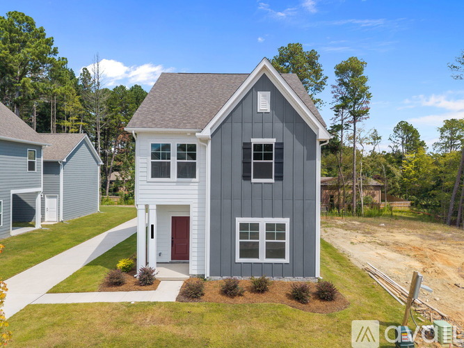 A grey house with a red door is surrounded by greenery.