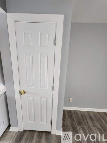 A white door with a gold handle is in a room with a wooden floor.