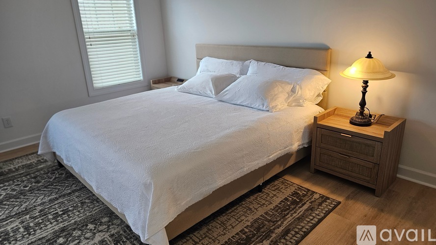 A bedroom with a large bed and a wooden nightstand with a lamp on it.