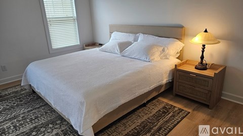 A bedroom with a large bed and a wooden nightstand with a lamp on it.