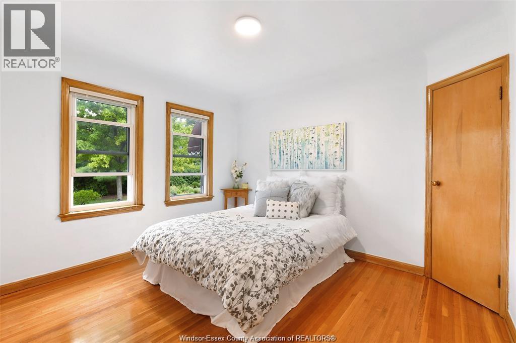 A bedroom with a bed, two windows, and a painting on the wall.