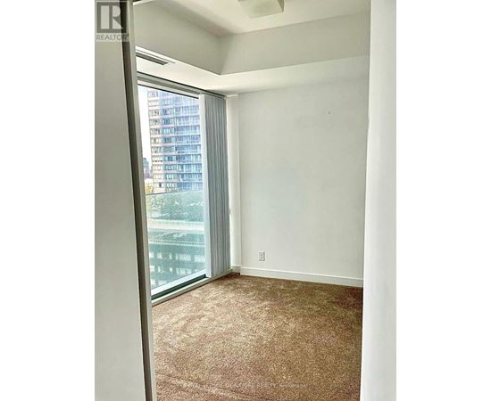 A room with a carpeted floor and a window with a view of a building outside.