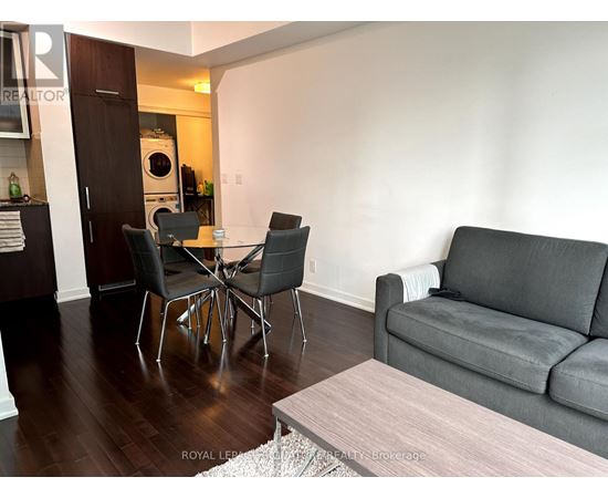 A grey couch sits in a living room with a coffee table and a dining table with chairs.