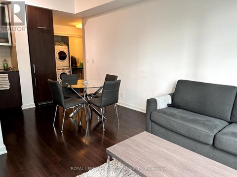 A grey couch sits in a living room with a coffee table and a dining table with chairs.